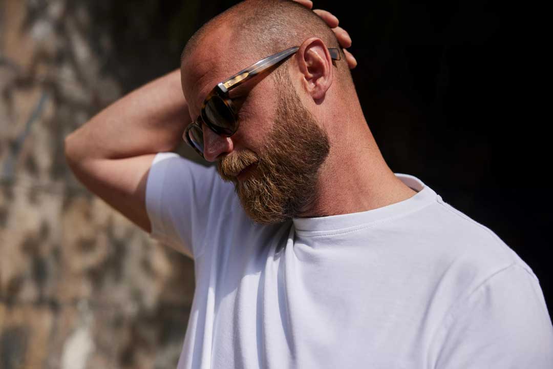 Side view of bearded man wearing tortoise shell sunglasses touching his head in bright sunlight