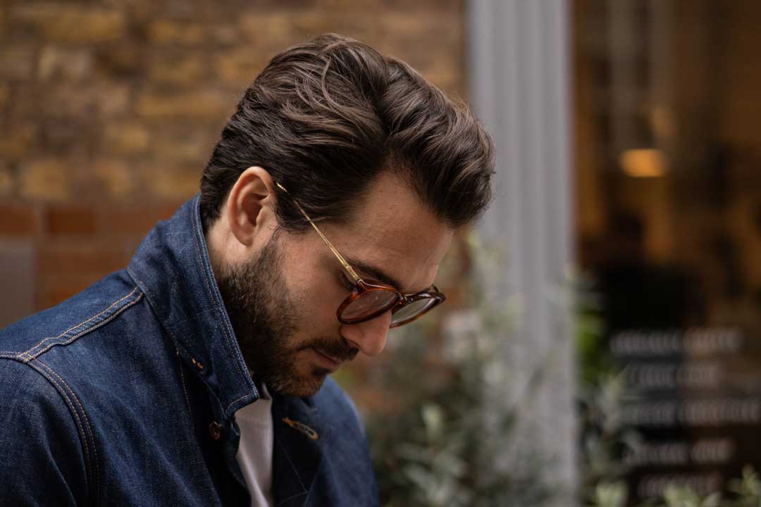 Side view of man in street wearing round amber eyeglasses looking downwards