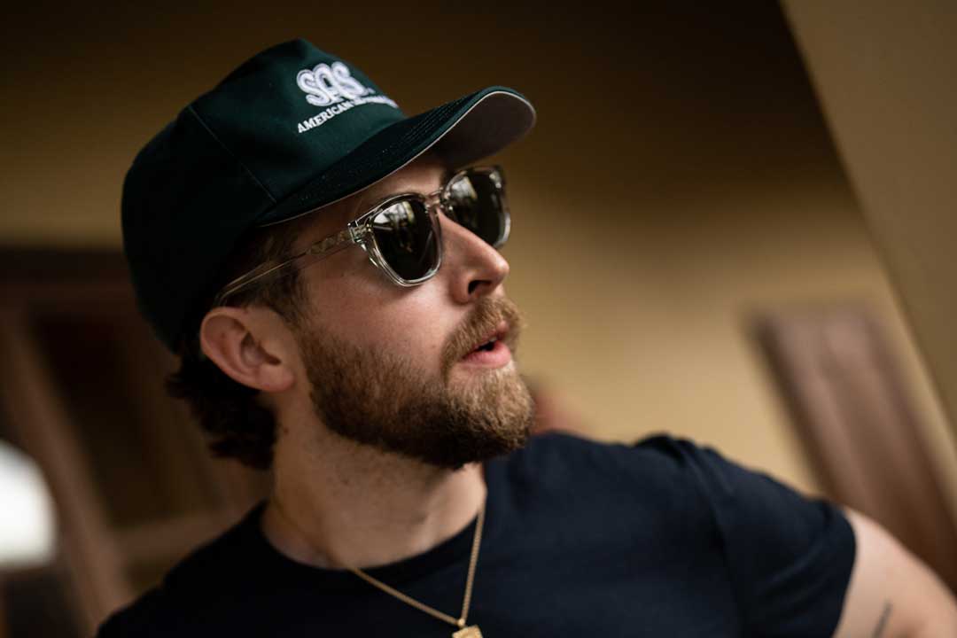 Side view of man wearing green cap and clear frame sunglasses