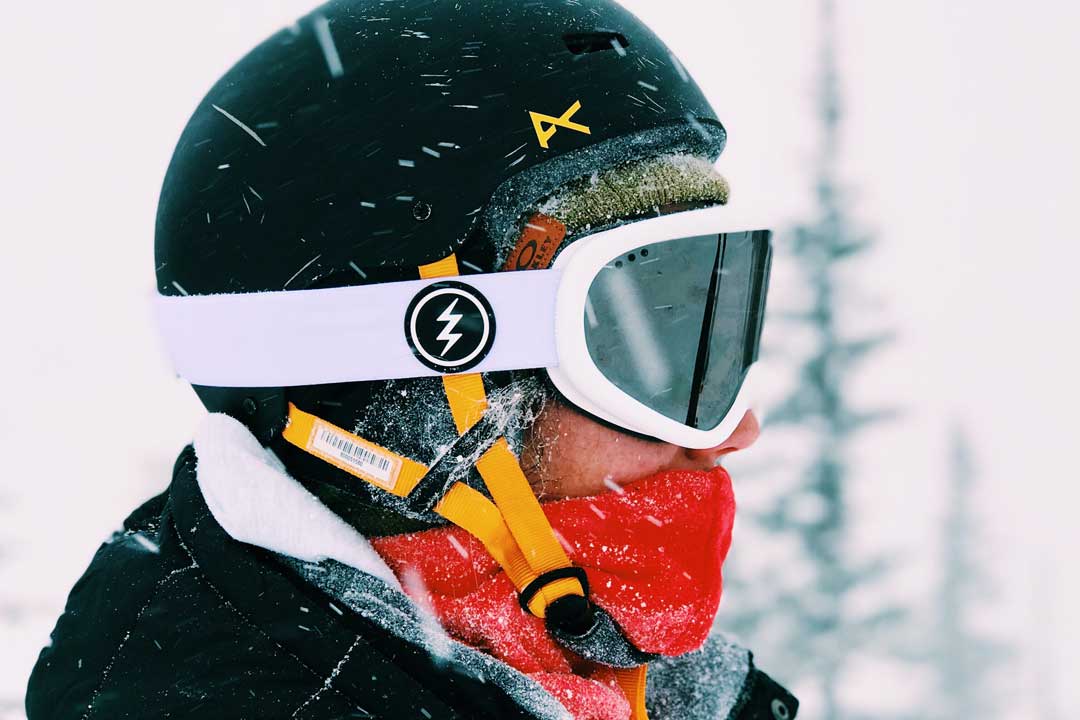 Side view of skier wearing black crash helmet and white ski goggles on a snowy day