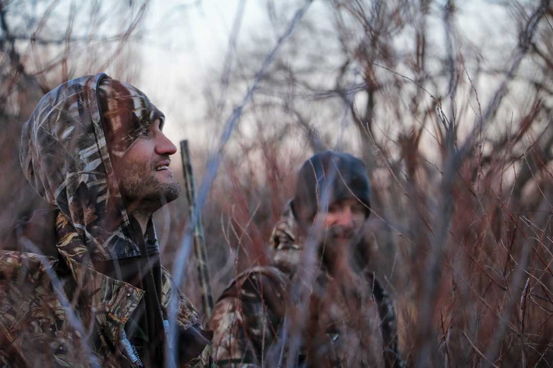 Side view of two men dressed in camouflage in dense woodland