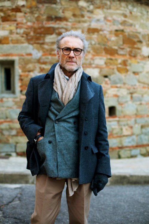 Smartly dressed man standing in front of an old building wearing winter clothes scarf and dark glasses frame