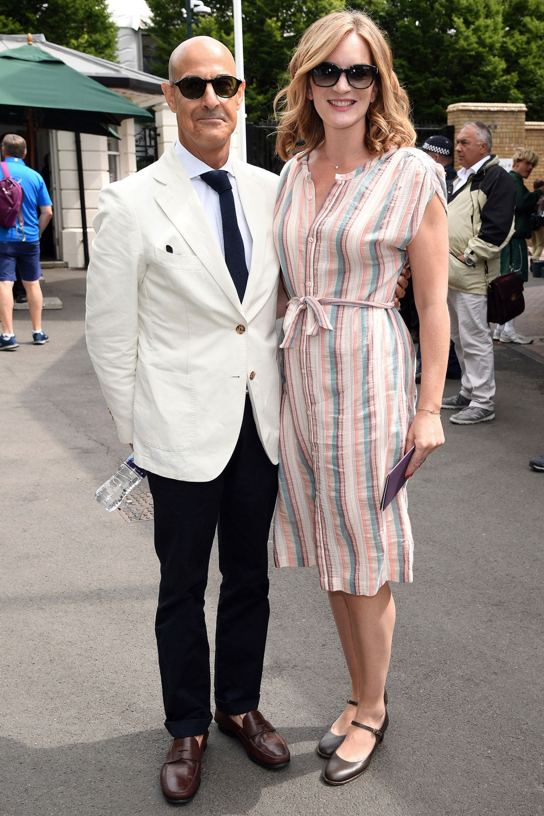 Stanley Tucci at Wimbledon wearing white suit sunglasses beside woman