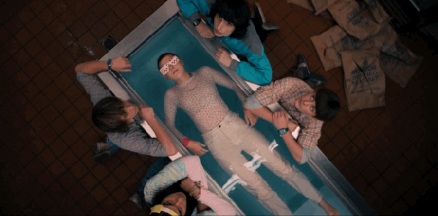 Stranger Things cast surrounding character Eleven whilst she floats in chest freezer filled with water