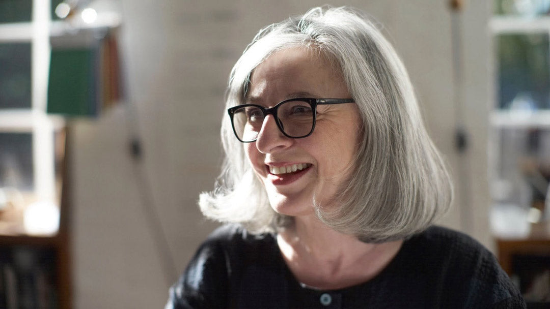 Three quarter view of a mature woman with a grey bob haircut and large black framed glasses