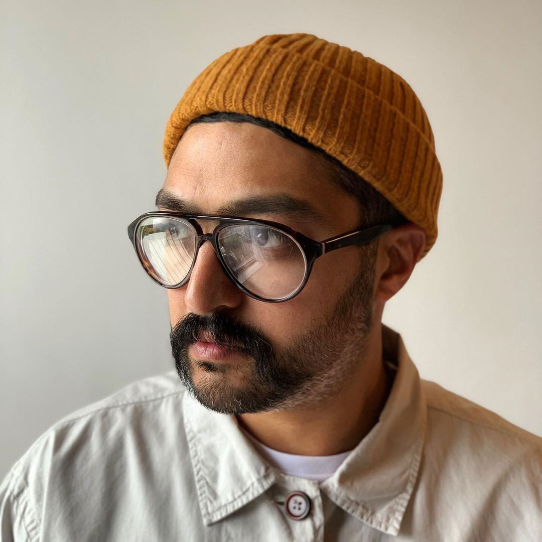 Three quarter view of a young bearded male with a round face wearing an orange hat and Aviator style eyeglasses