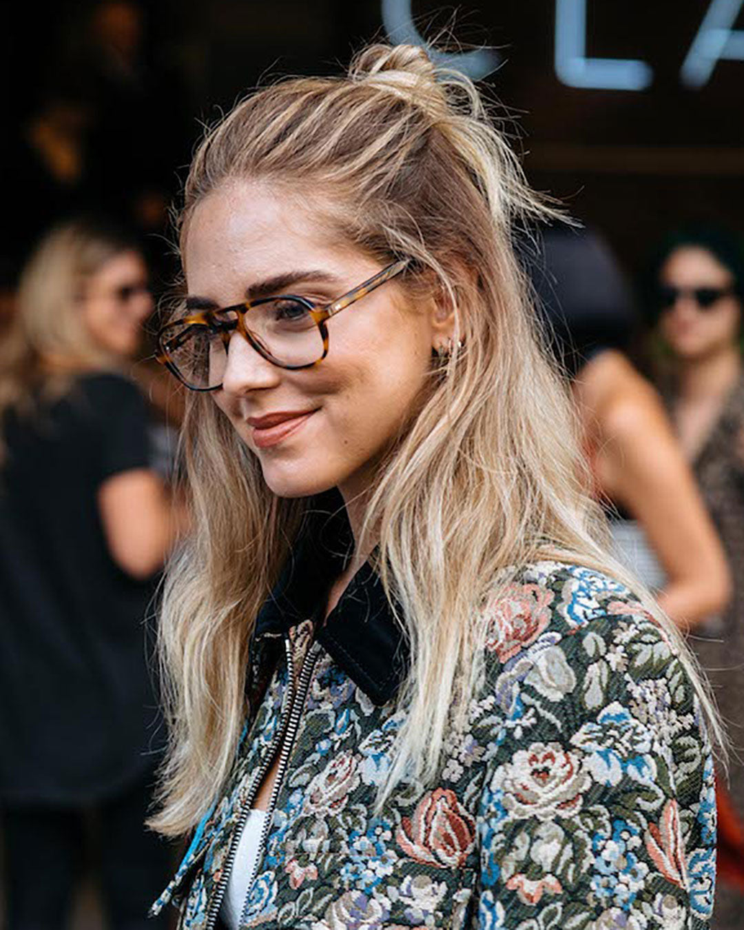 Three quarter view of blonde lady in floral top and large tortoise glasses frame