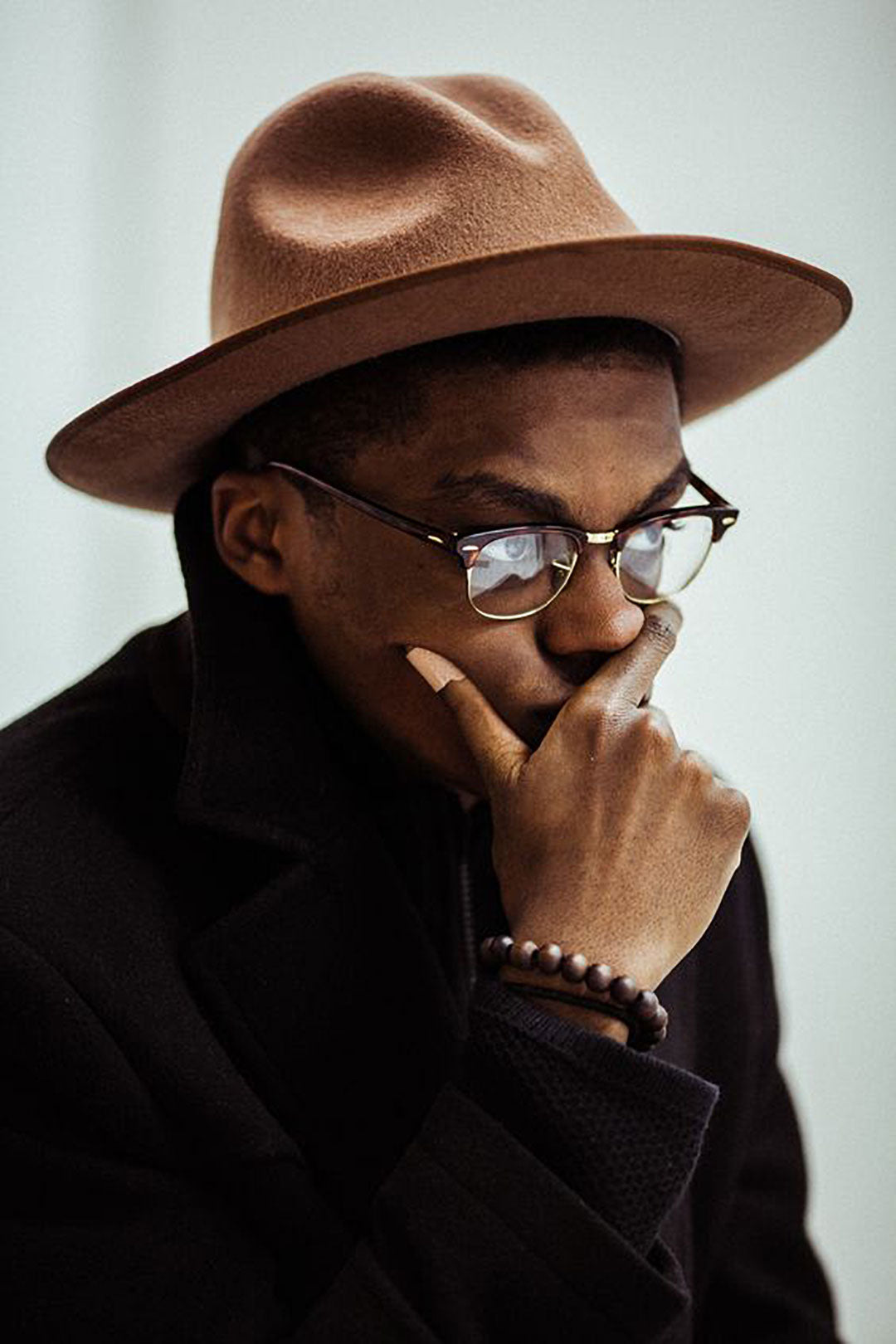 Three quarter view of man in brown hat and browline glasses frame touching his face