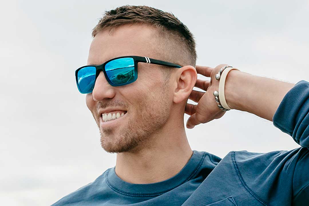 Three quarter view of man smiling wearing black sunglasses frame with blue mirror lenses