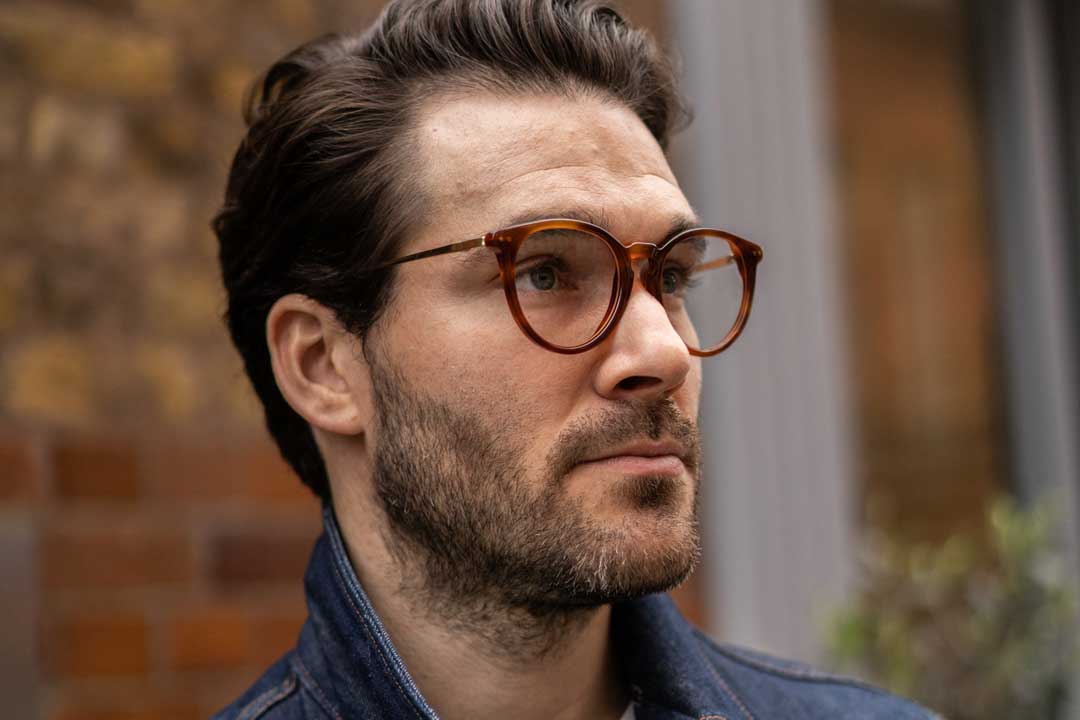 Three quarter view of man wearing round amber eyeglasses outside in street