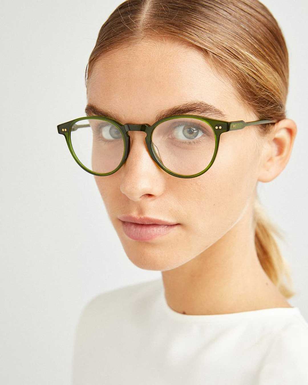 Three quarter view of young woman wearing round green eyeglasses frame and white shirt