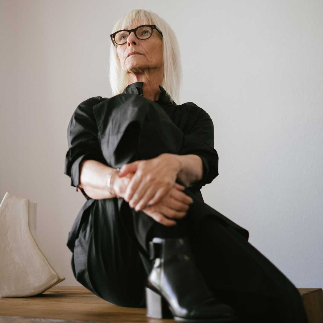 Upward view of mature woman sitting on top of desk wearing dark clothes and eyeglasses frame