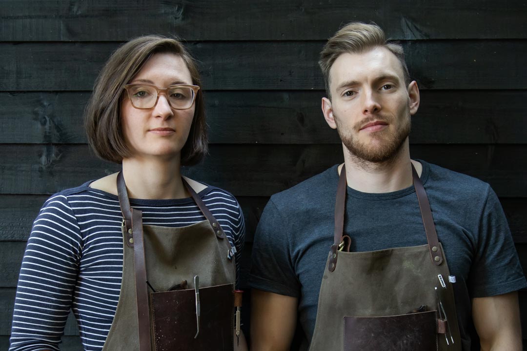 Woman and man standing together in front of black wall wearing aprons