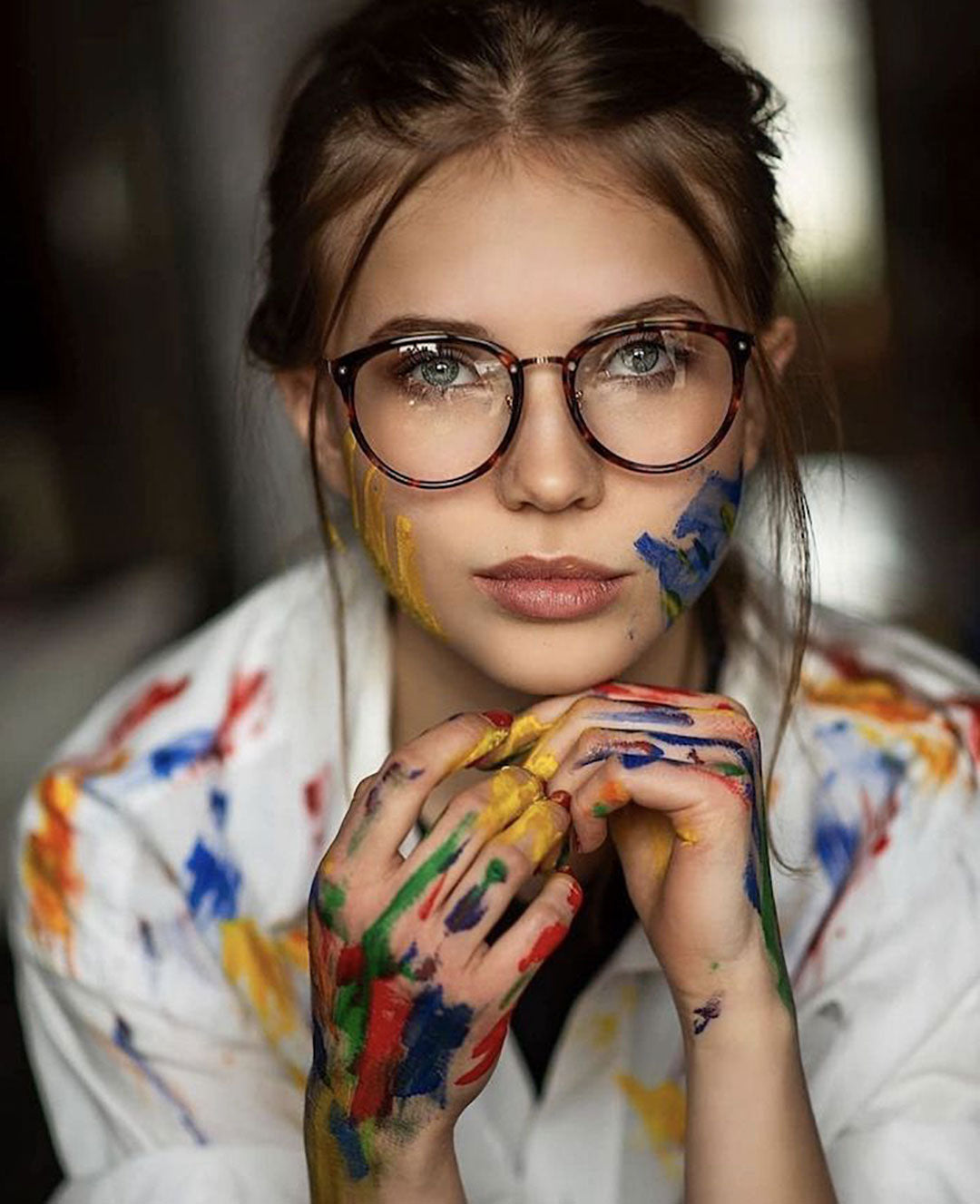 Woman in round eyeglasses covered in different colours of paint