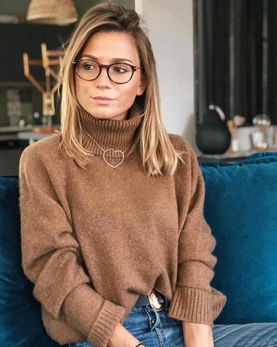 Woman on sofa looking sideways wearing brown jumper and spectacles frame