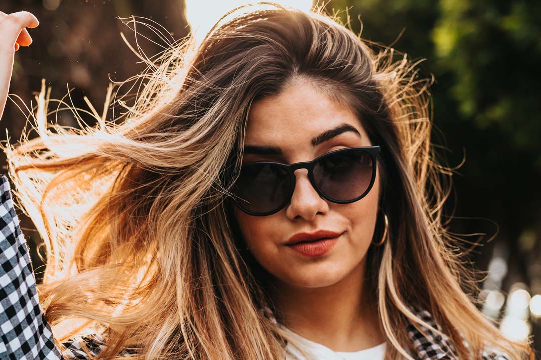 Woman outside on sunny day wearing oval black sunglasses and checked shirt