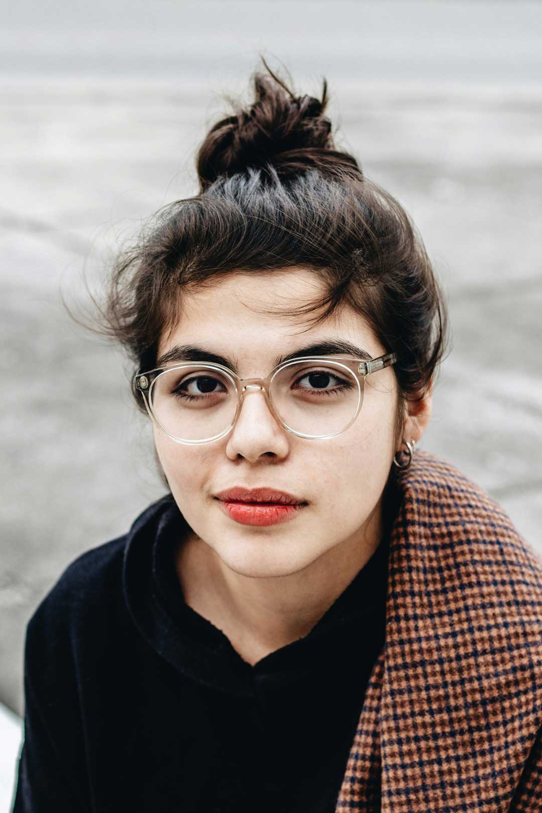 Woman sitting outside wearing tweed jacket and clear frame eyeglasses