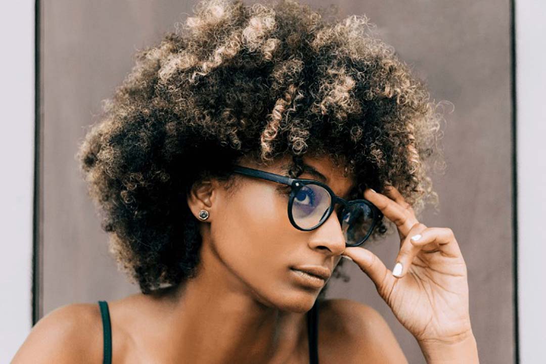 Woman with afro haircut touching her thick round eyeglasses