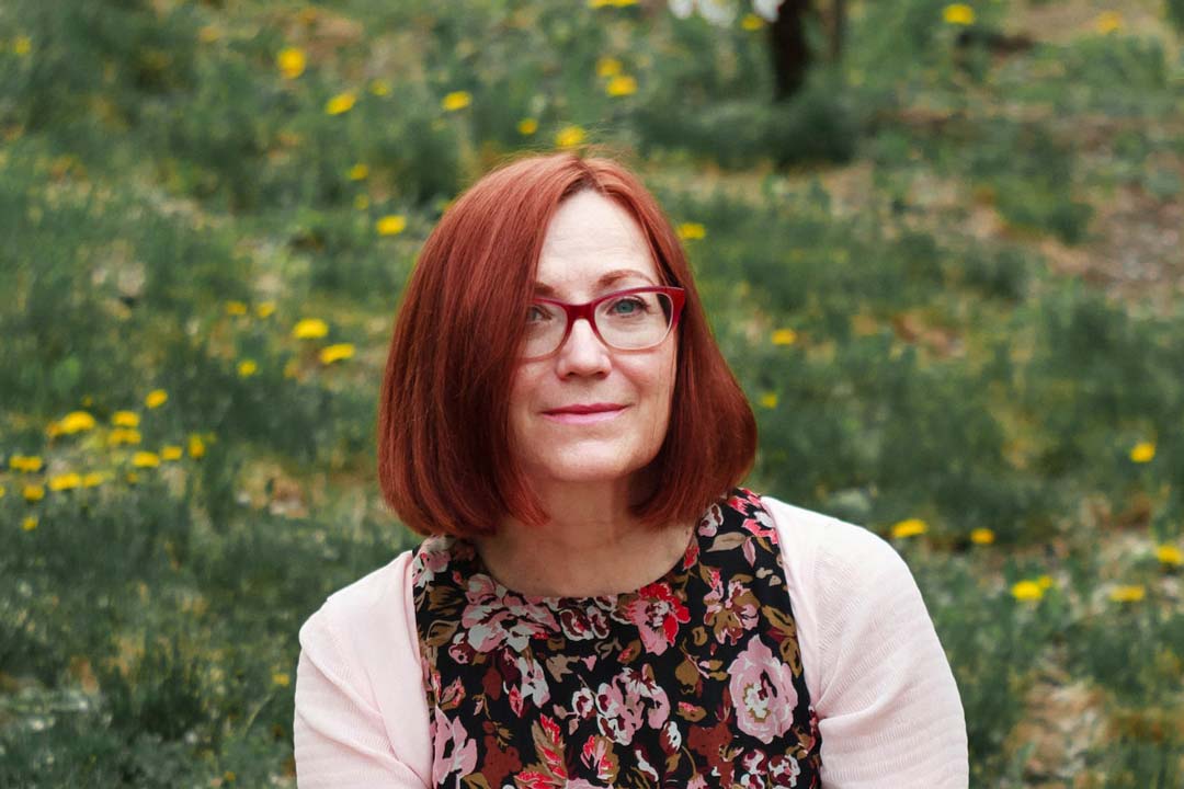 Woman with red hair and red eyeglasses sitting in meadow outside on sunny day