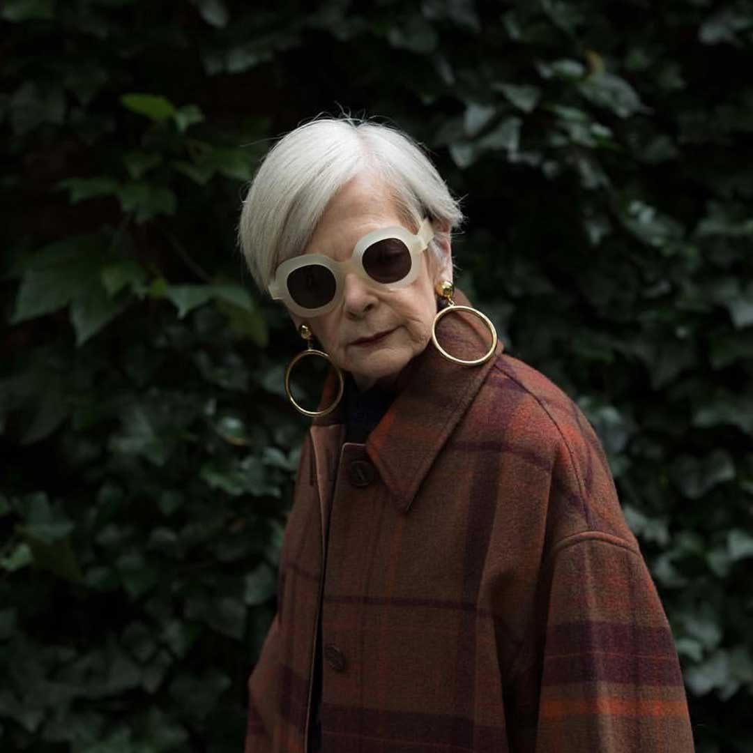 Woman with short grey bob haircut wearing white frame sunglasses and thick wool coat