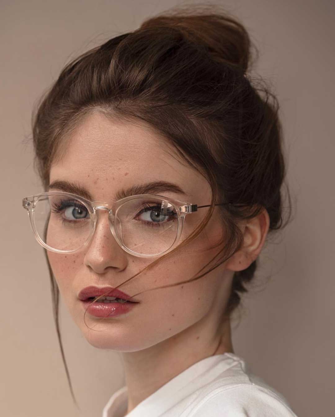 Woman with tied up brown hair wearing white shirt and clear eyeglasses frame