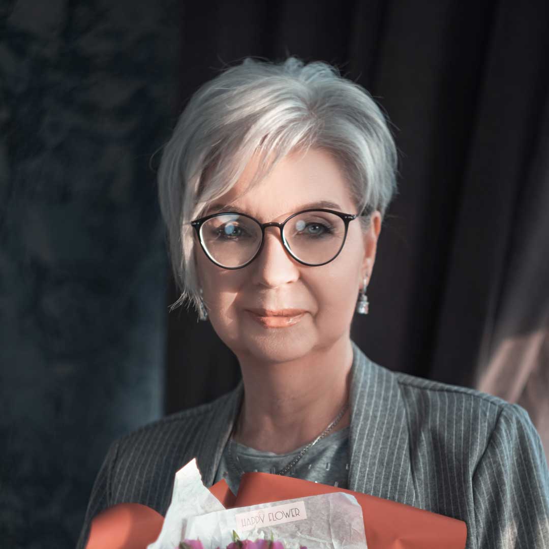 Woman with with grey pixie haircut holding bouquet of flowers in dark room