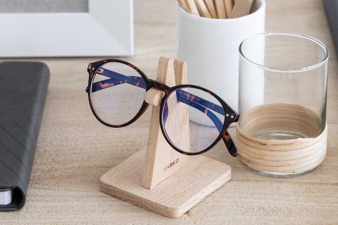 Wooden spectacle holder stand on desk beside computer and pen pot