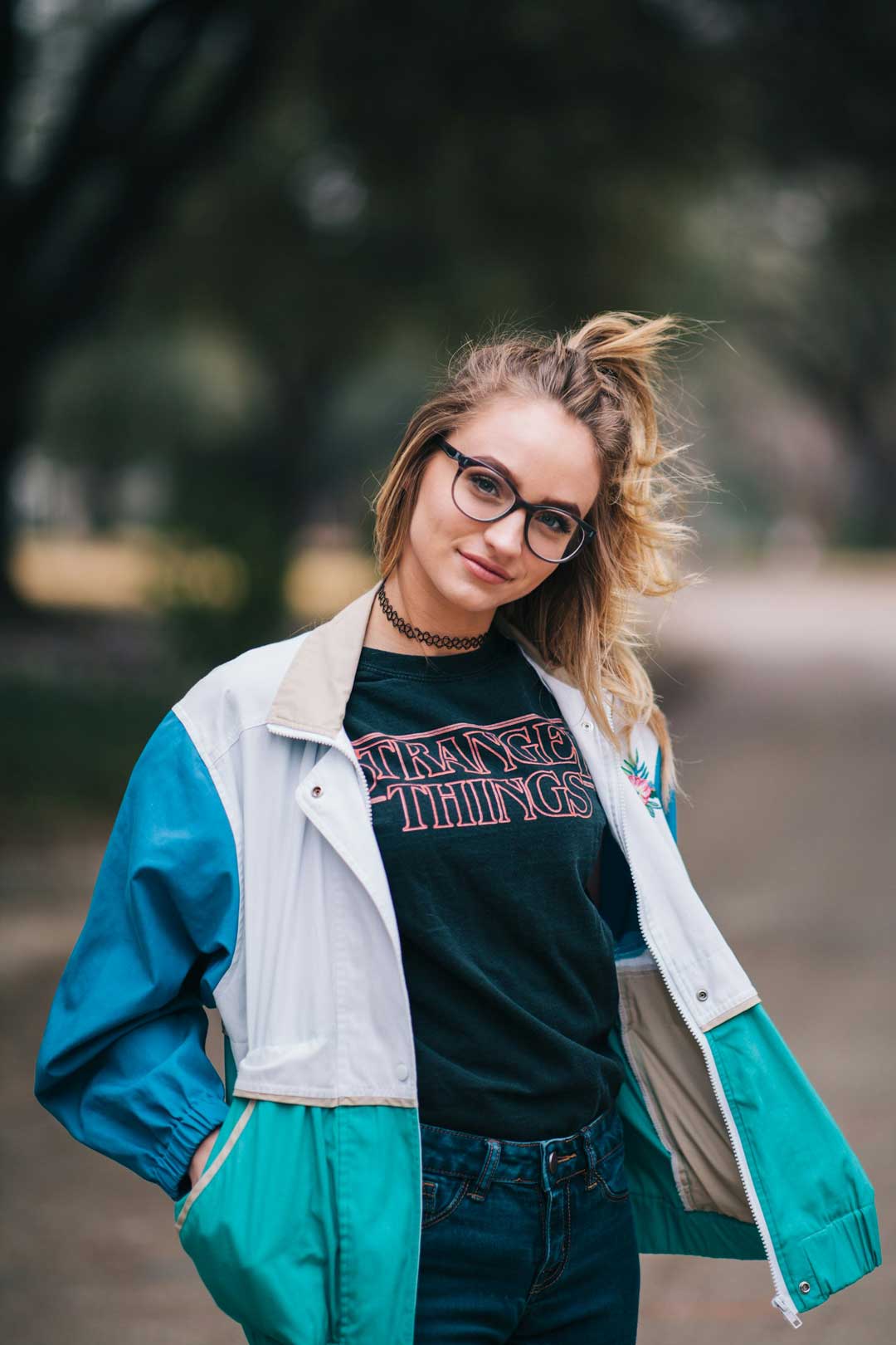 Yound-blonde-female-wearing-turquoise-jacket-and-thick-rimmed-eyeglasses-outside-on-sunny-day