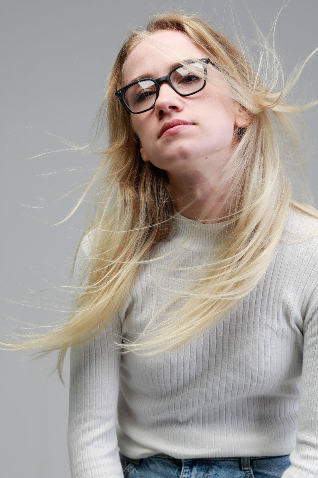 Young  female with dark square glasses with her blonde hair being blown about