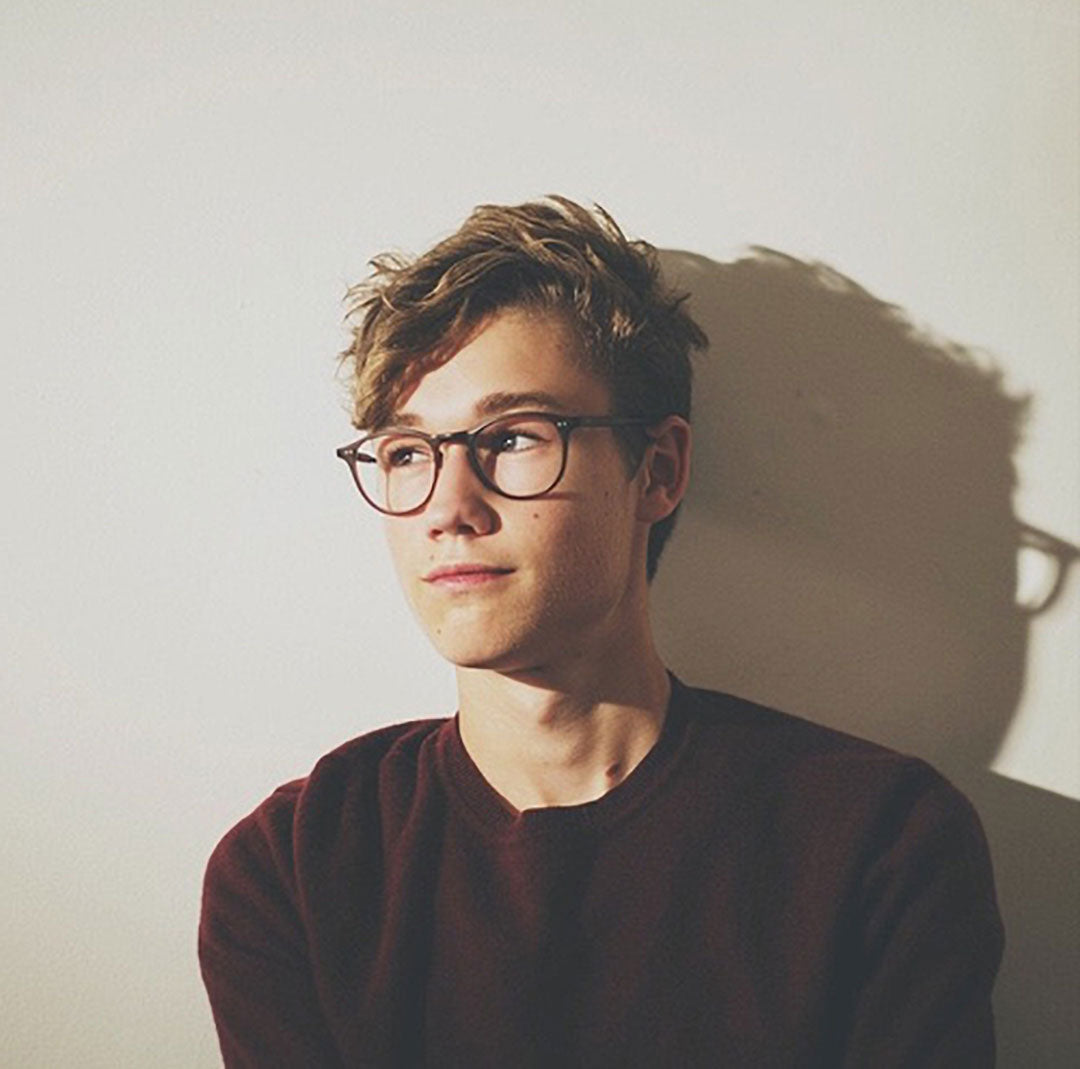 Young guy with blonde hair looking sideways through round brown eyeglasses