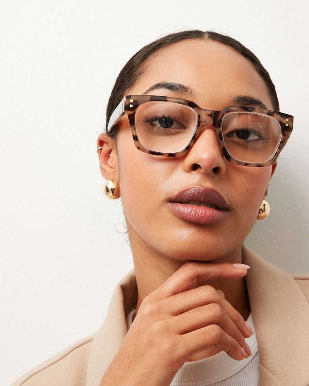 Young lady wearing thick torotise glasses and cream sweater looking directly at viewer