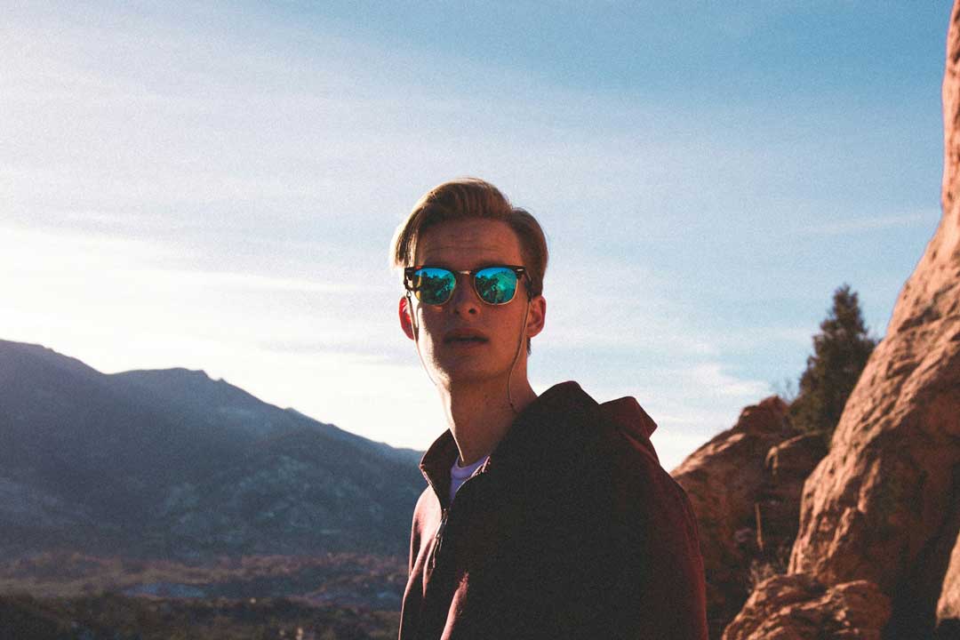Young man in mountains on sunny day wearing blue mirrored sunglasses frame