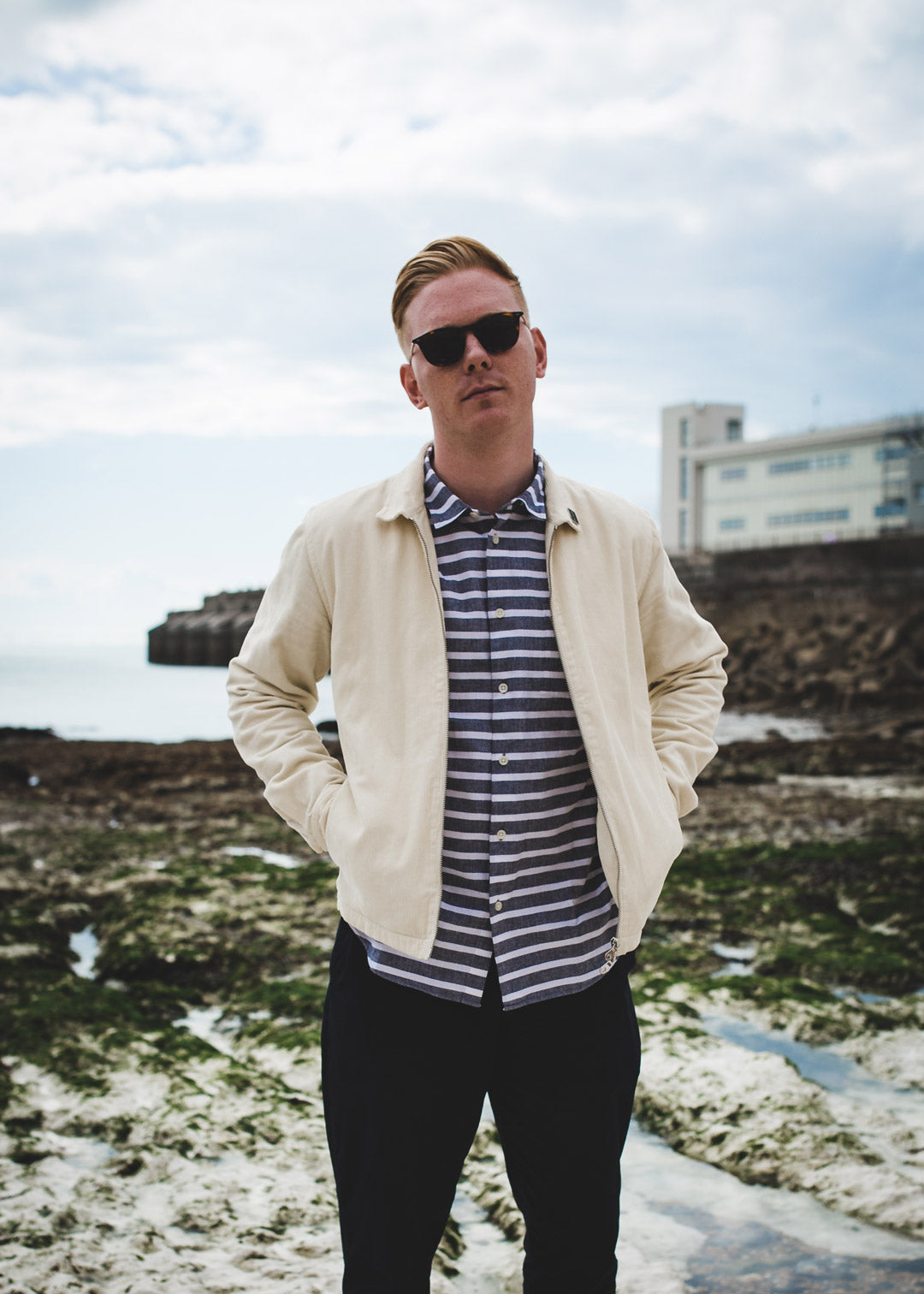 Young man standing at the beach wearing sunglasses with the sea behind him