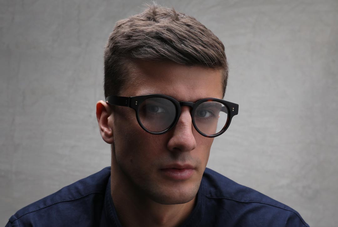 Young man with square face wearing thick round eyeglasses and blue shirt