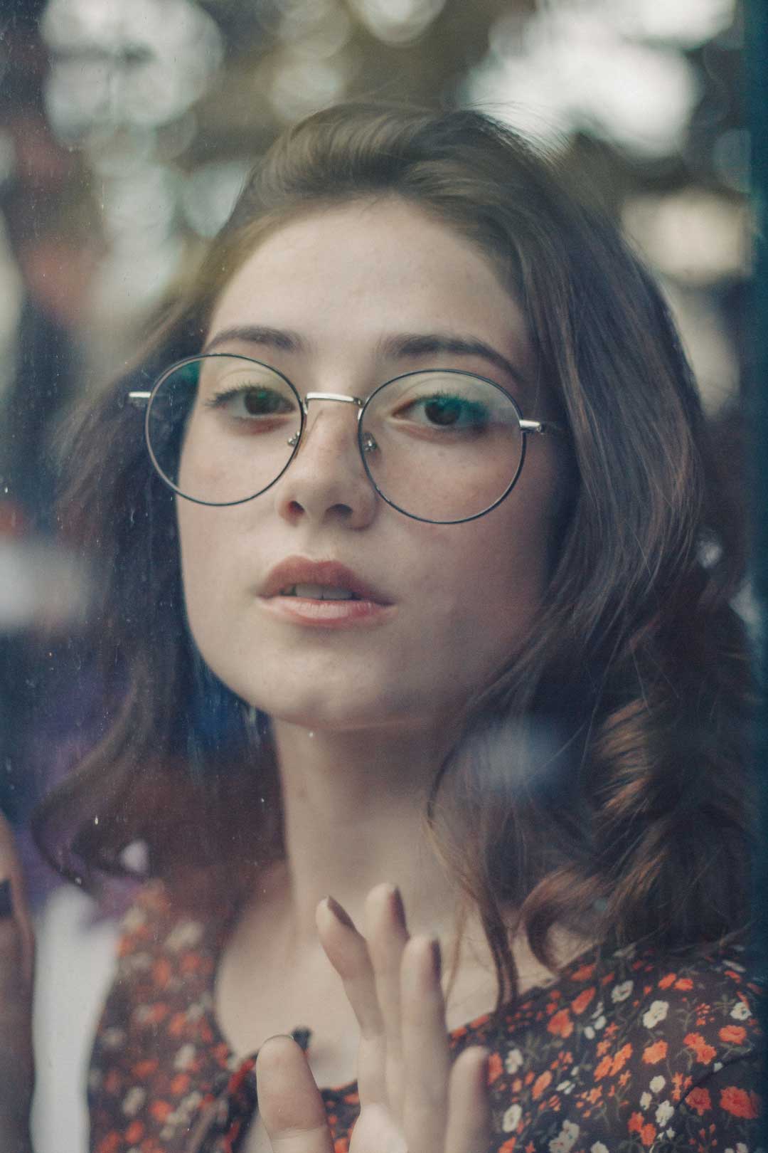 Young woman behind glass window wearing round wire rimmed eyeglasses frame