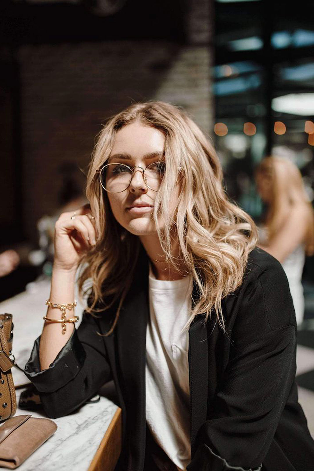 Young woman leaning on marble bar top wearing black top and round wire glasses frame