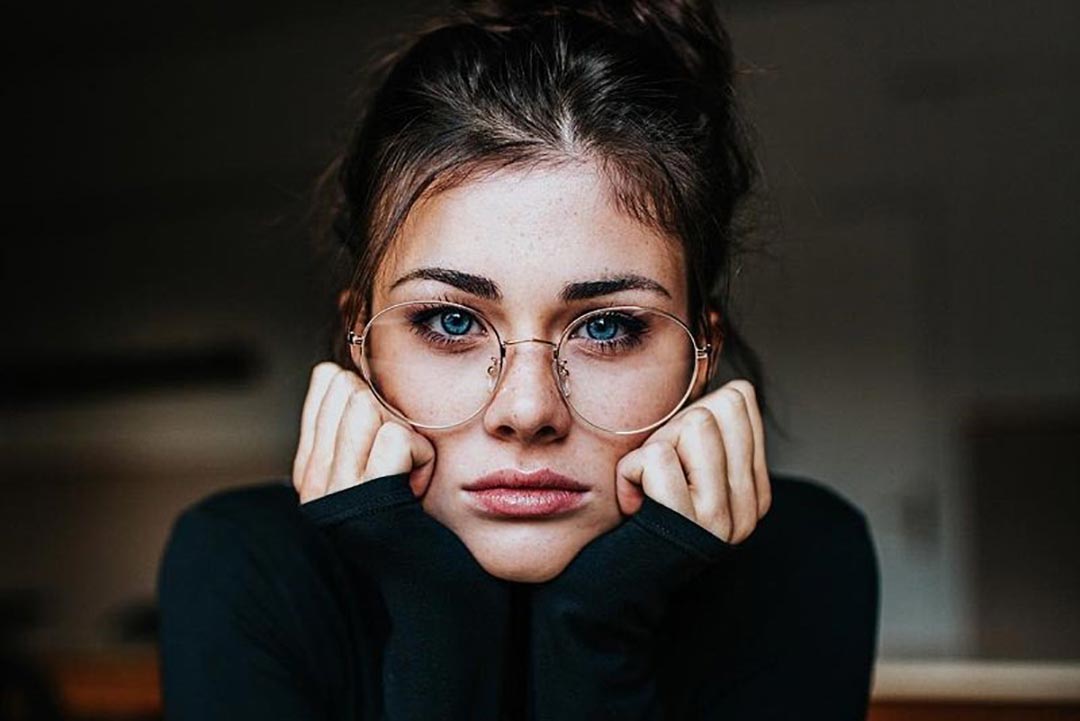 Young woman resting her head in her hands wearing very large round wire spectacles