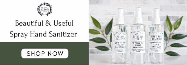 3 bottles of hand sanitizer spray with essential oils for scent including lavender citrus, rosemary white thyme, and peppermint eucalyptus pictured in front of a laurel wreath and white and gray marble backsplash