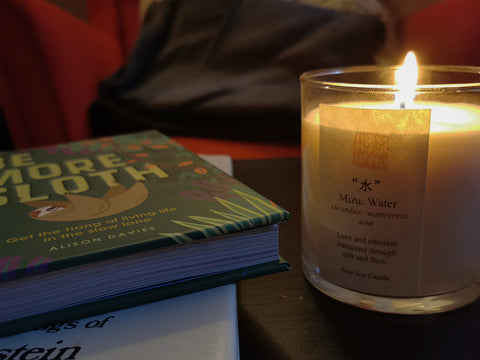 Photo of a cozy reading area with lit candle and Be More Sloth book