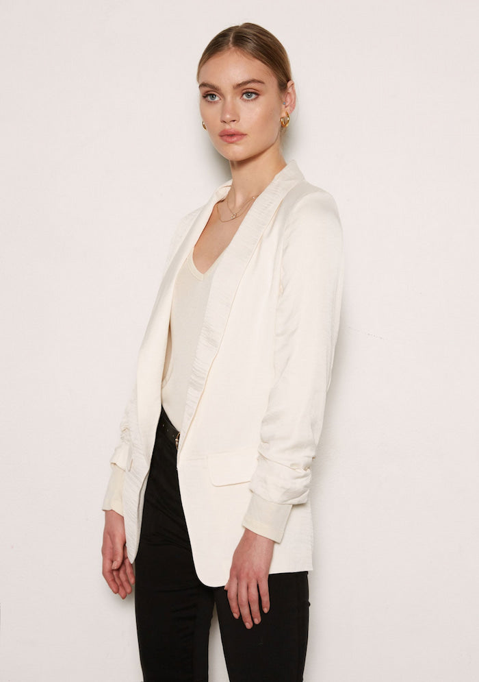 A woman in a chic work outfit consisting of a white blazer and a black pant.