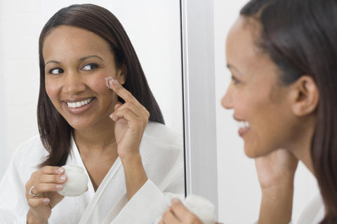 woman looking in the mirror and applying skin care cream