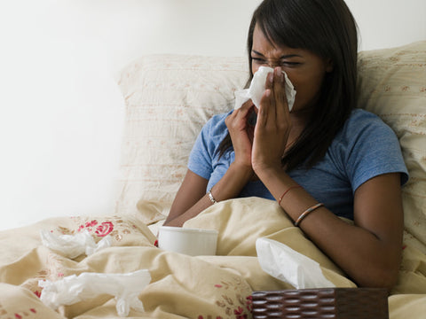 woman sitting up in bed blowing her nose which causes dry skin around nose