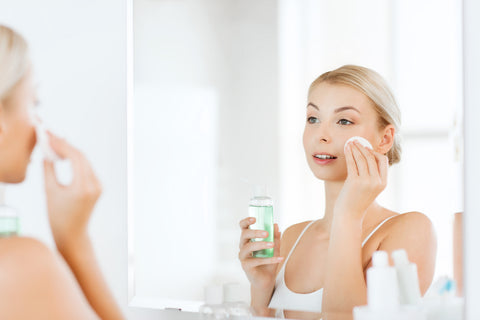 woman looking in mirror and applying toner to her face