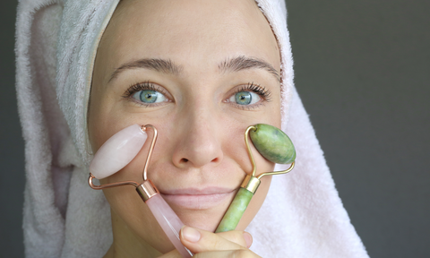 woman holding jade face roller and rose quartz face roller