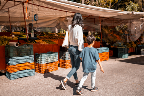 Young mother walks with child through outdoor market.