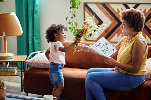 Young child hands bouquet of flowers to older woman holding a Mother's Day card.