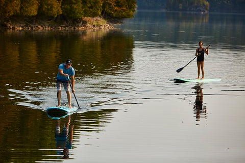 A couple stand up paddle boarding on a lake