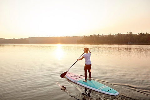 a female paddle boarding at sunset