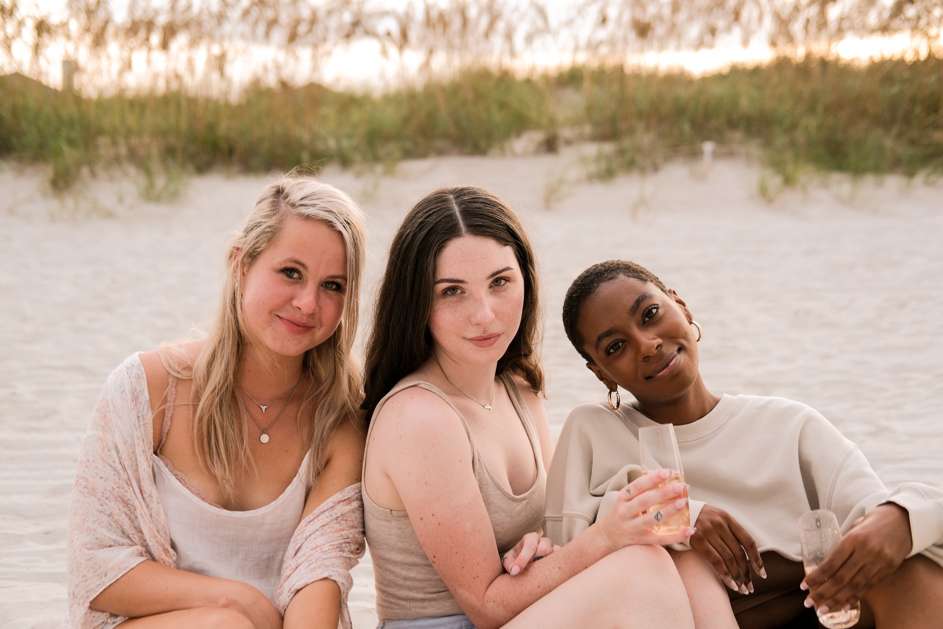 Community of women hanging out on the beach during sunset drinking champagne and having a jolly good time. Beautiful lighting - lots of earth tones. 