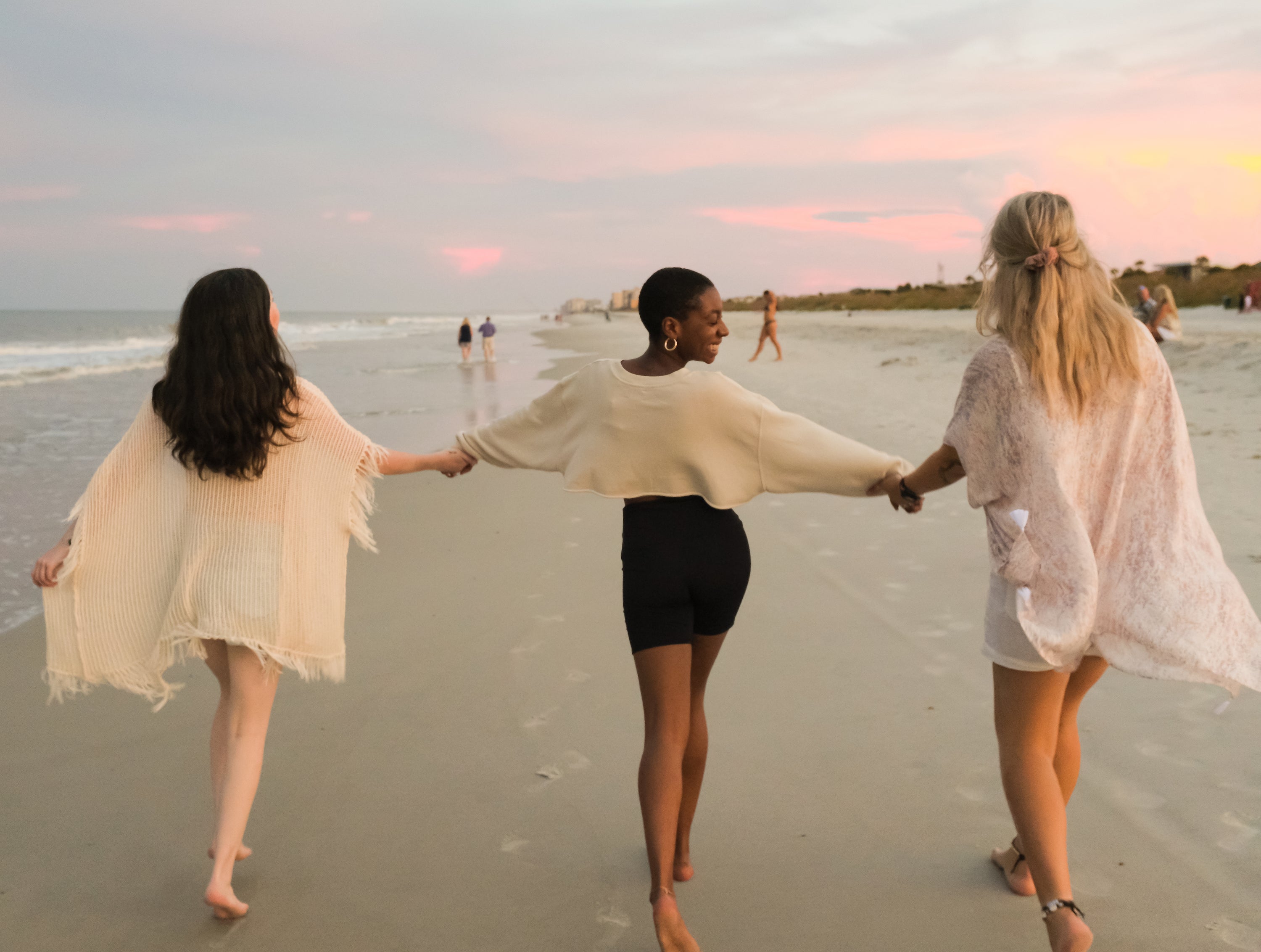 East Coast Beach in the USA at Sunset with three best friends holding hands and skipping down the beach. Pink hues, relaxing vibe. 
